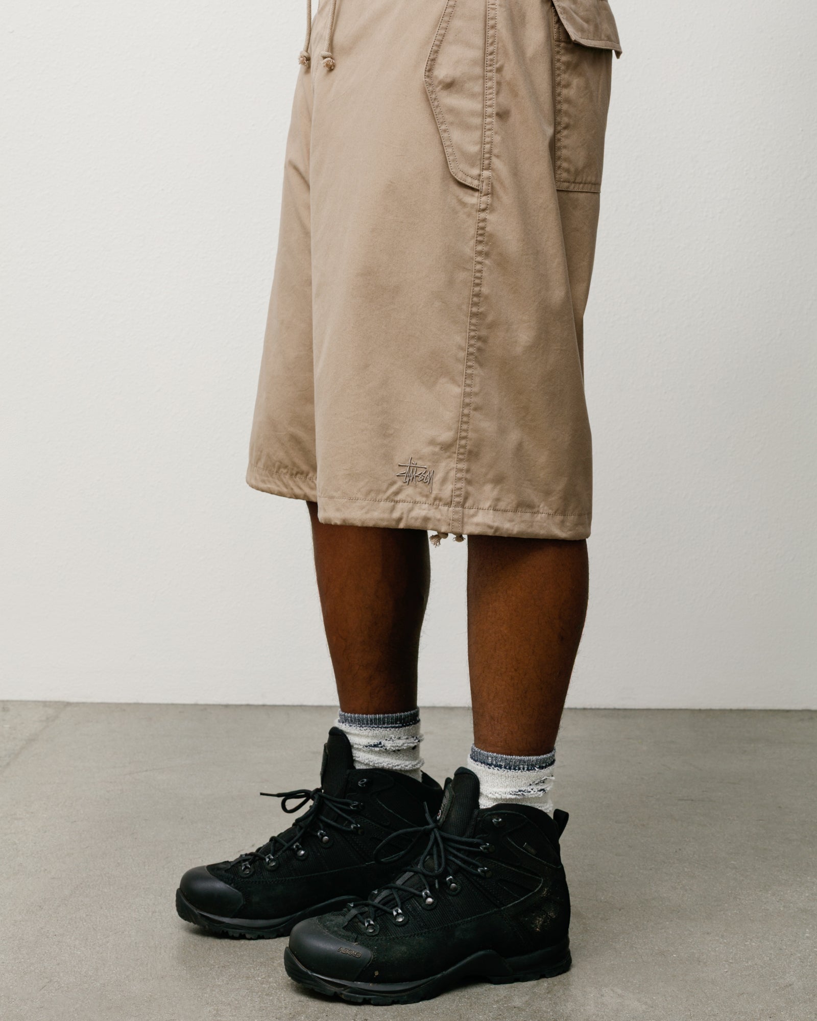 카키 색상 코튼‑나일론 배기 쇼츠, 밑단 드로코드와 Stüssy 로고, 워커 부츠와 스타일링