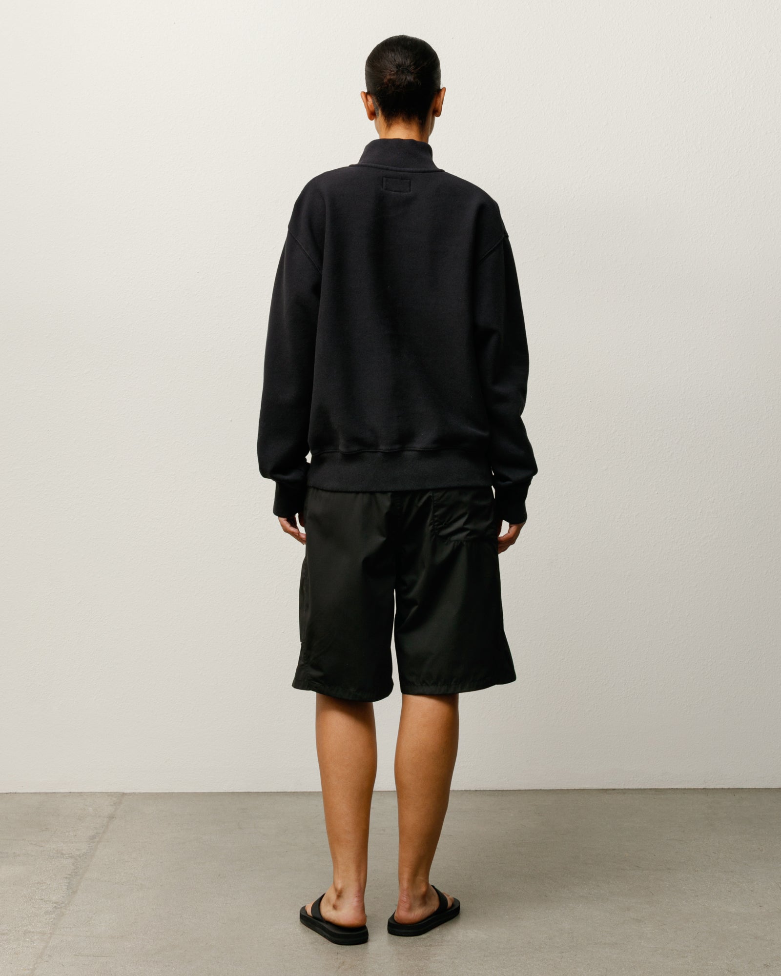 스투시(Stüssy)의 블랙 컬러 커브드 패널 보드 쇼츠 남성용 레귤러 피트 하의를 착용한 모델의 뒷모습으로 여유로운 실루엣과 깔끔한 디자인이 특징입니다.
