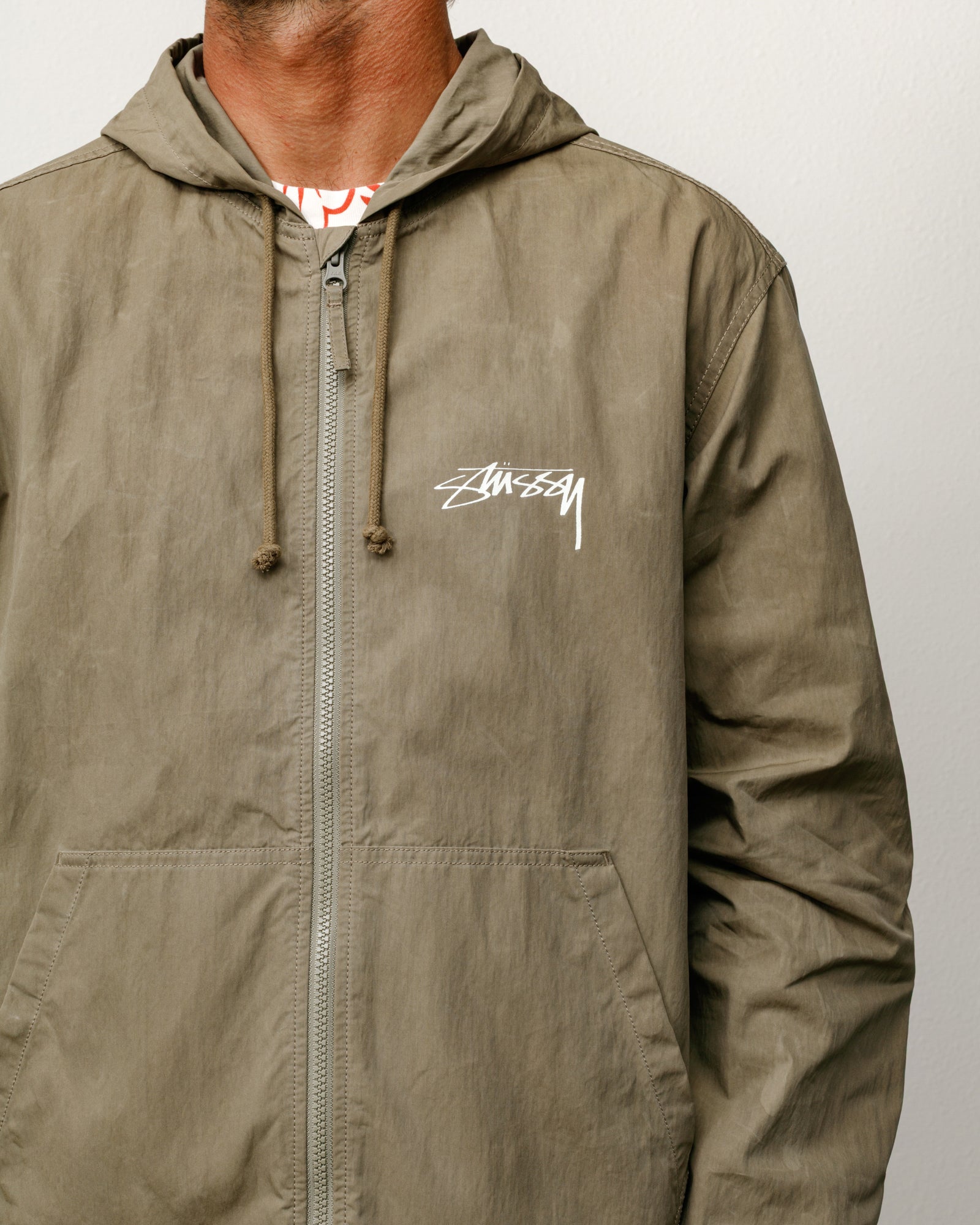 올리브 컬러의 왁스드 코튼 비치 쉘 아우터웨어 재킷, 후드와 지퍼 여밈, 가슴의 Stüssy 로고