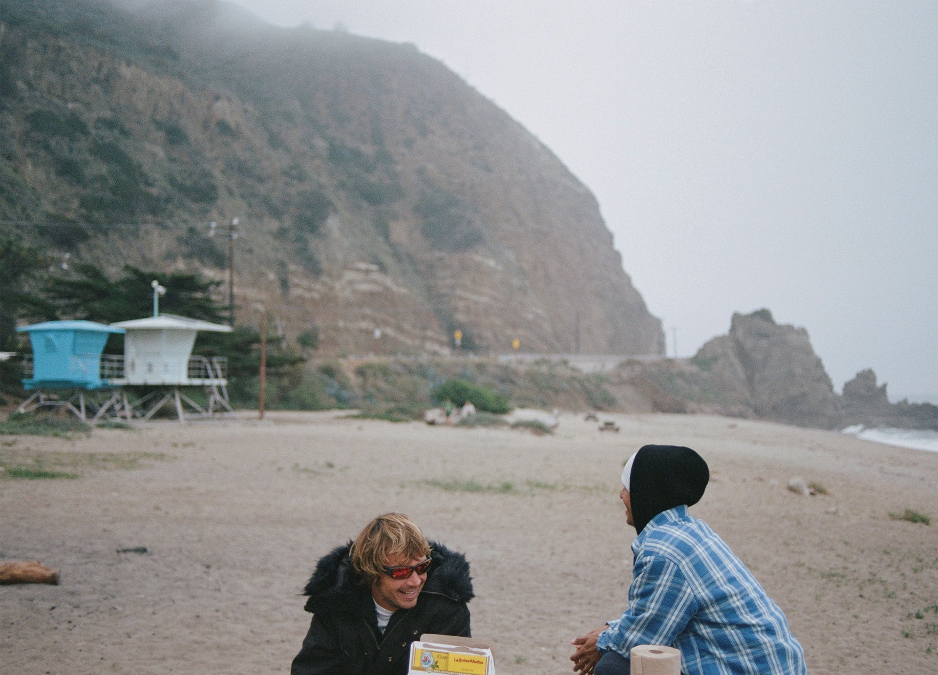 Two people sitting on a beach with a mountain in the background