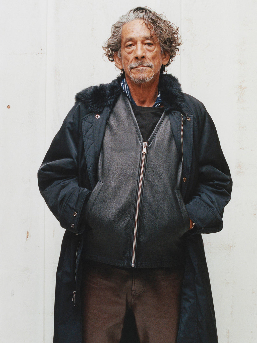 Model wears the Stüssy Pile Lined Leather Vest in Black layered under a long black coat with brown trousers.